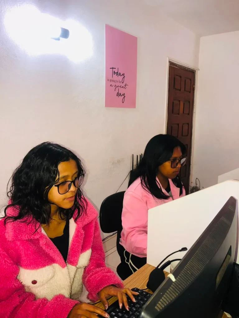 Deux femmes travaillant sur des ordinateurs dans un bureau, avec un message inspirant au mur sur une journée réussie.