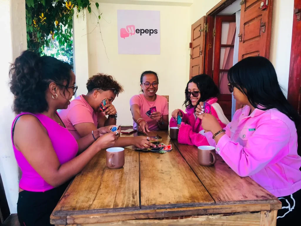 Cinq personnes en rose jouent à des cartes autour d'une table, illustrant un moment convivial et collaboratif.